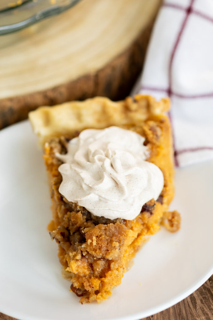 A front view of a piece of southern sweet potato pie on a white plate topped with a swirl of whipped cream.
