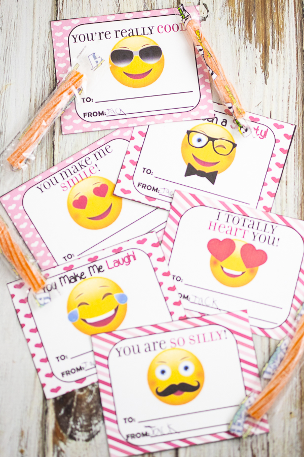 Cut out emoji valentines on a white wood background with orange sour straws