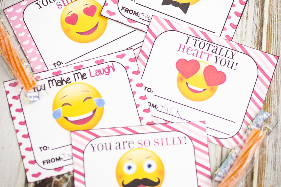 Cut out emoji valentines on a white wood background with orange sour straws