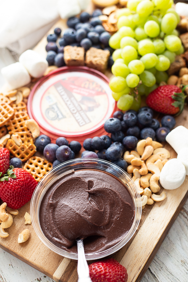 Dessert charcuterie board including dark chocolate hummus, blueberries, strawberries, grapes, pretzels, cookies, banana bread, cashews, and marshmallows.