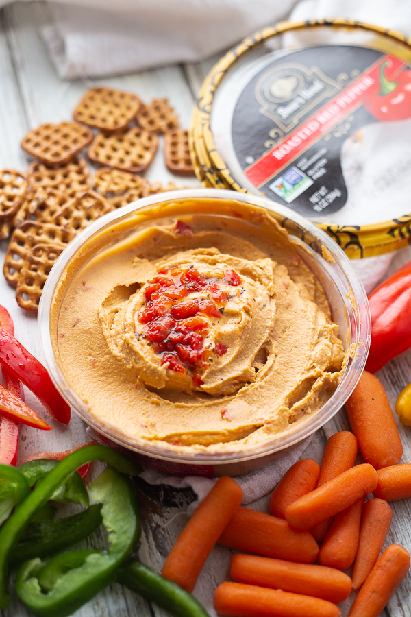 Boar's Head Roasted Red Pepper Hummus on a white wood background with mini peppers, pretzels, carrots, and bell peppers