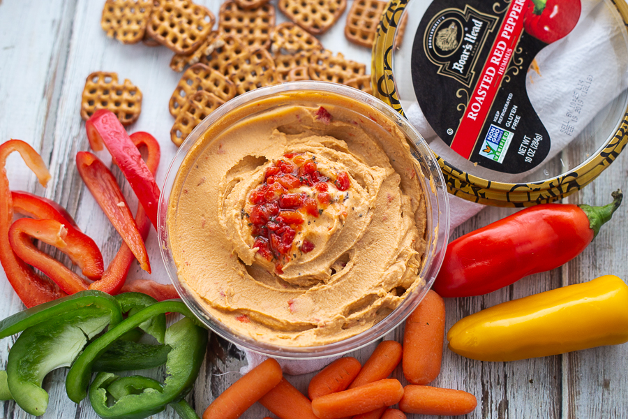 Boar's Head Roasted Red Pepper Hummus on a white wood background with mini peppers, pretzels, carrots, and bell peppers