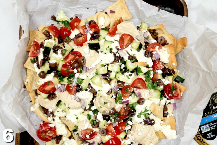 Fully assembled Greek Nachos with toppings on parchment paper