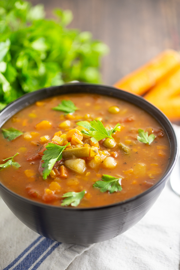 Homemade Vegetable Soup in a matte black bowl with parsley and carrots in the background.