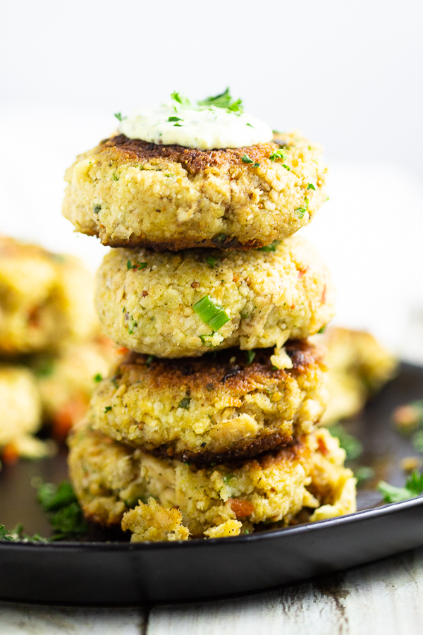 Four salmon croquettes stacked in a tower on a black plate with remoulade and parsley on top