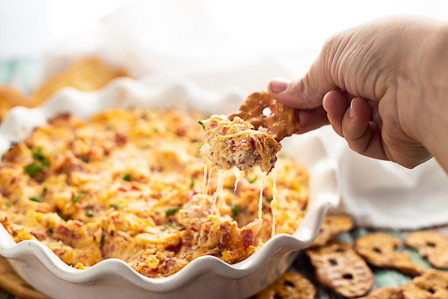 Reuben dip in a white ruffled pie dish with a pretzel chip being dipped in