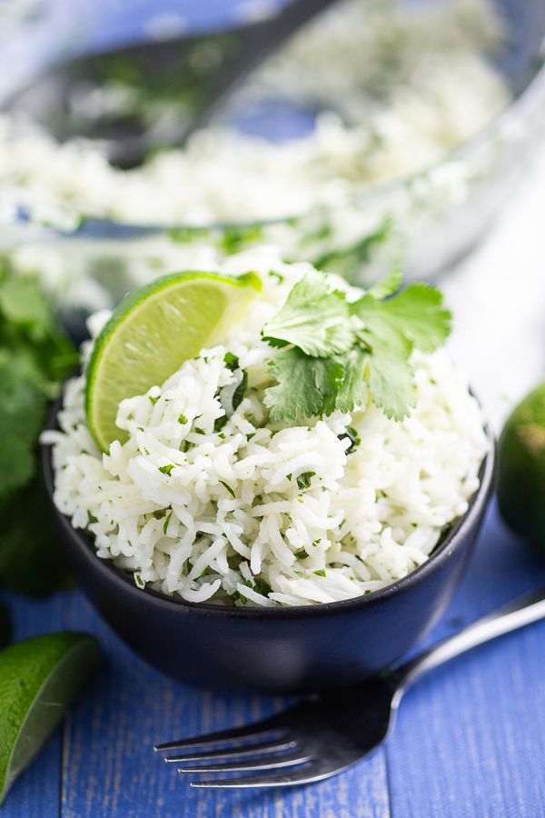 White chipotle lime rice garnished with a fresh lime wedge and sprig of cilantro in a black bowl on a blue wood background