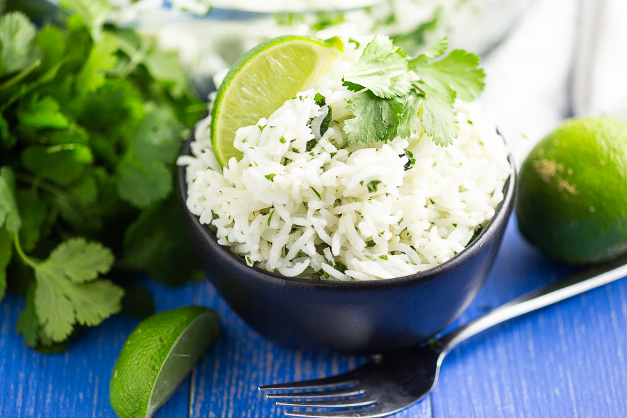 White chipotle lime rice garnished with a fresh lime wedge and sprig of cilantro in a black bowl on a blue wood background