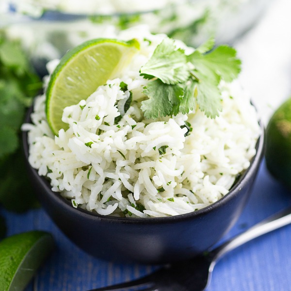 White chipotle lime rice garnished with a fresh lime wedge and sprig of cilantro in a black bowl on a blue wood background