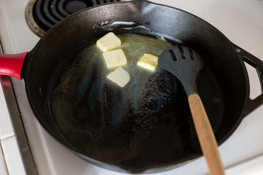 Butter melting in a cast iron skillet on a white electric stove