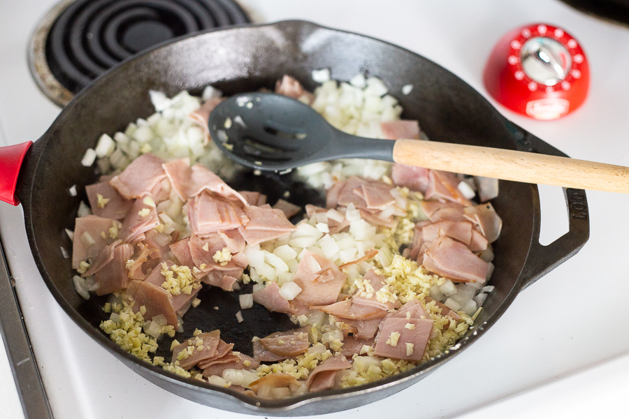 Ham, chopped onion, and minced garlic in a cast iron skillet being stirred together