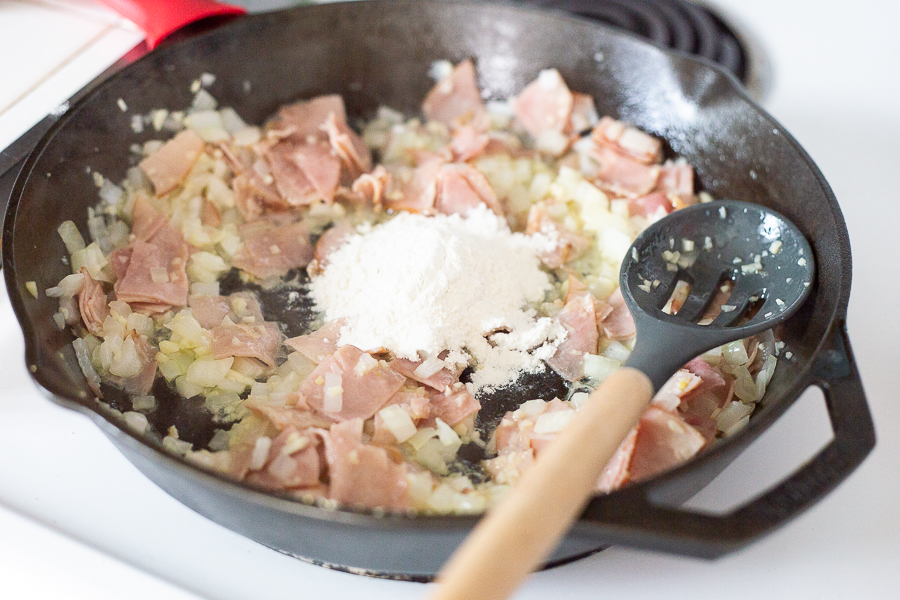 Flour being added to ham, onion, and garlic mixture in the cast iron skillet