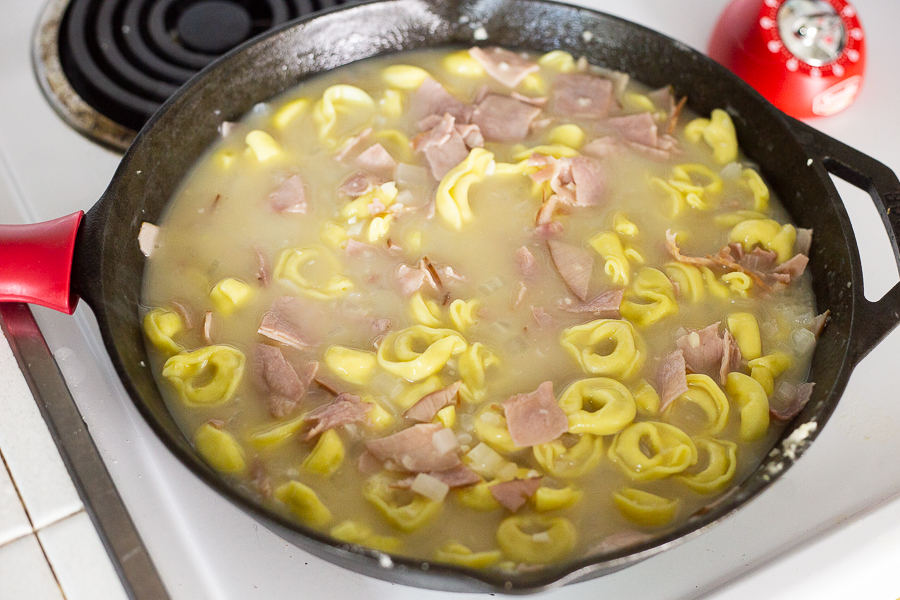Tortellini simmering in ham and broth mixture in a cast iron skillet