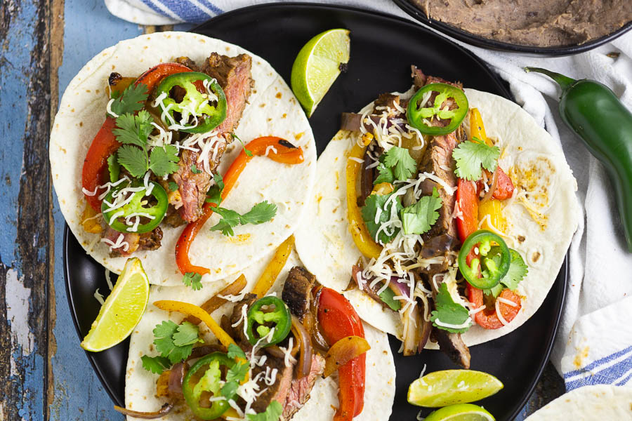 Steak fajitas with flour tortillas on a black plate on a blue distressed wood backgroud