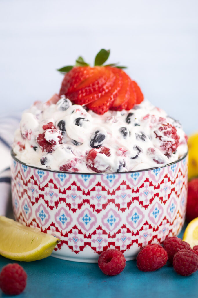 Berry cheesecake salad topped with a sliced strawberry next to a lemon wedge and fresh raspberries