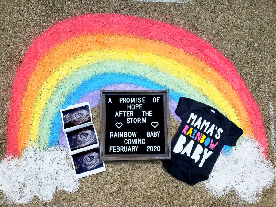 Rainbow drawn in chalk on a sidewalk with an ultrasound, a sign, and a onesie