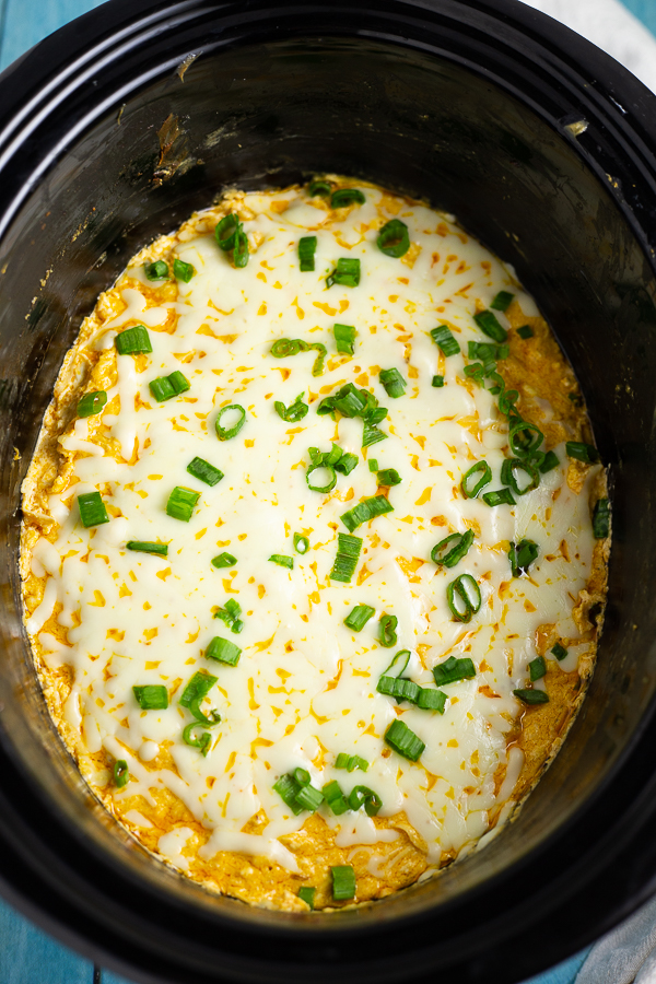 Crockpot buffalo chicken dip in a black slow cooker with melted mozzarella and sliced green onions on top.