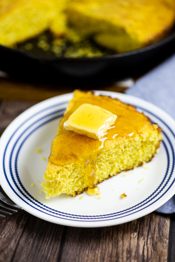 Wedge of cornbread topped with a pat of butter and honey on a white and blue plate on a rustic wood background