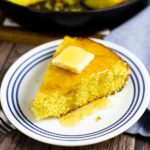 Wedge of cornbread with butter and honey on a white and blue plate on a rustic wood background.