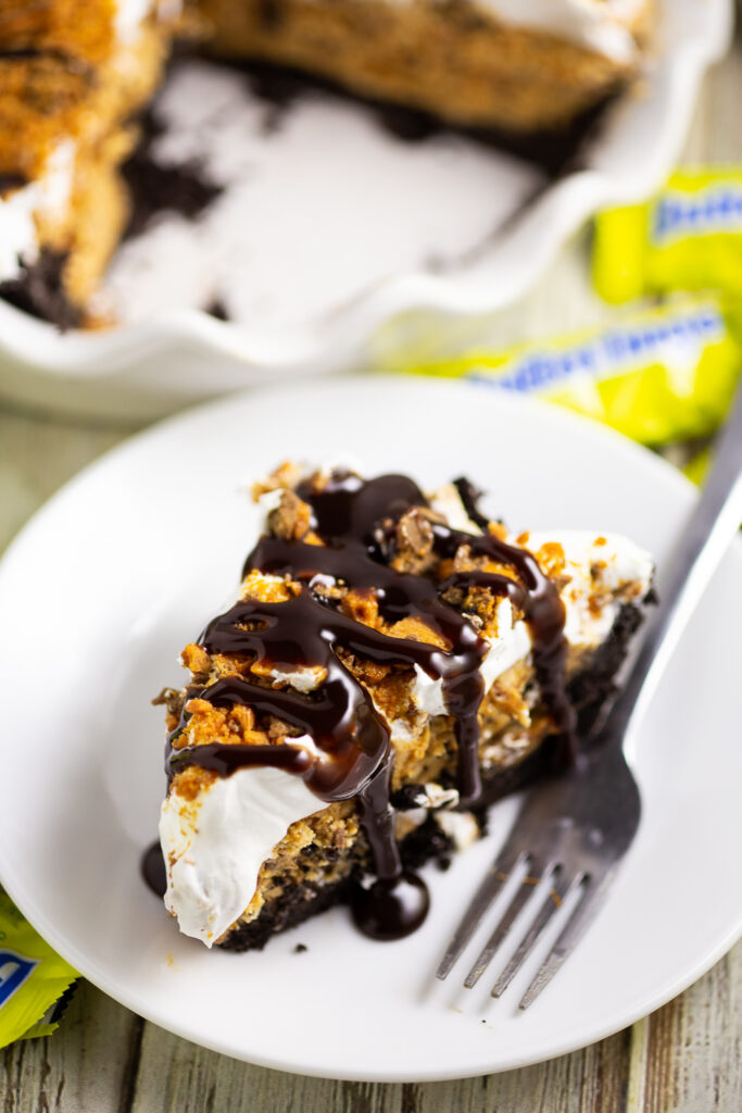 Slice of Butterfinger pie on a small plate with a fork and fun size Butterfingers in the background