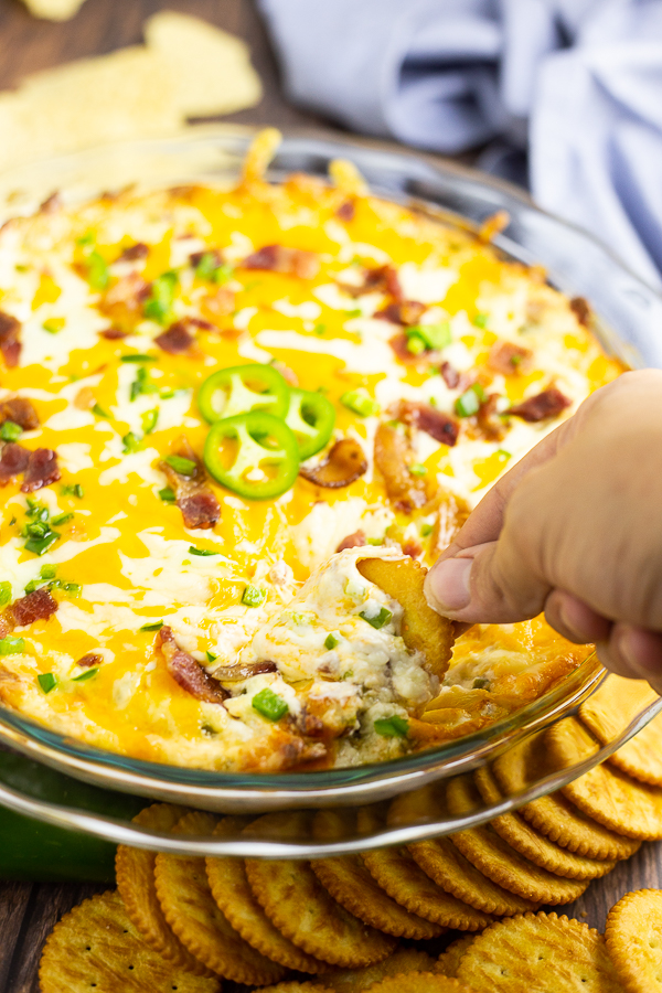 Butter cracker being dipped into jalapeno popper dip