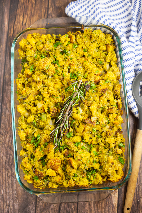 Cornbread dressing in a glass dish with a rosemary sprig on top on a rustic wood background