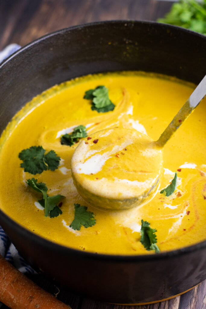 Curried carrot soup in a large cast iron pot with a ladle taking a scoop from the middle.