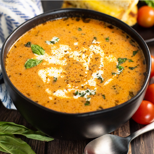 Black bowl of creamy tomato basil soup with fresh basil and cream swirled on top