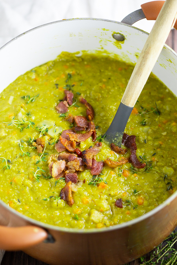 Split pea soup in a copper pot topped with bacon with a wooden spoon in the middle