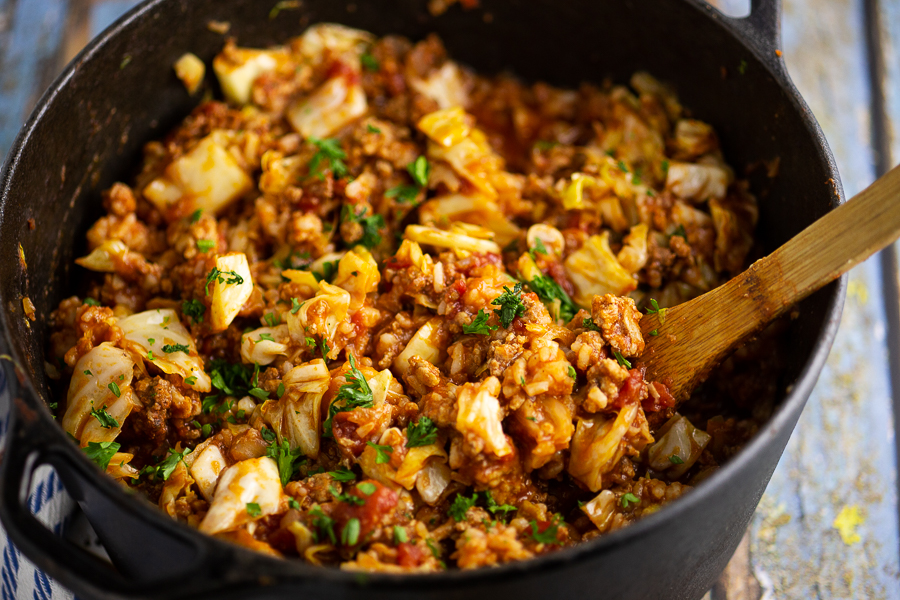 Unstuffed cabbage rolls in a black cast iron Dutch oven with a wooden spoon in the middle on a rustic wood background.