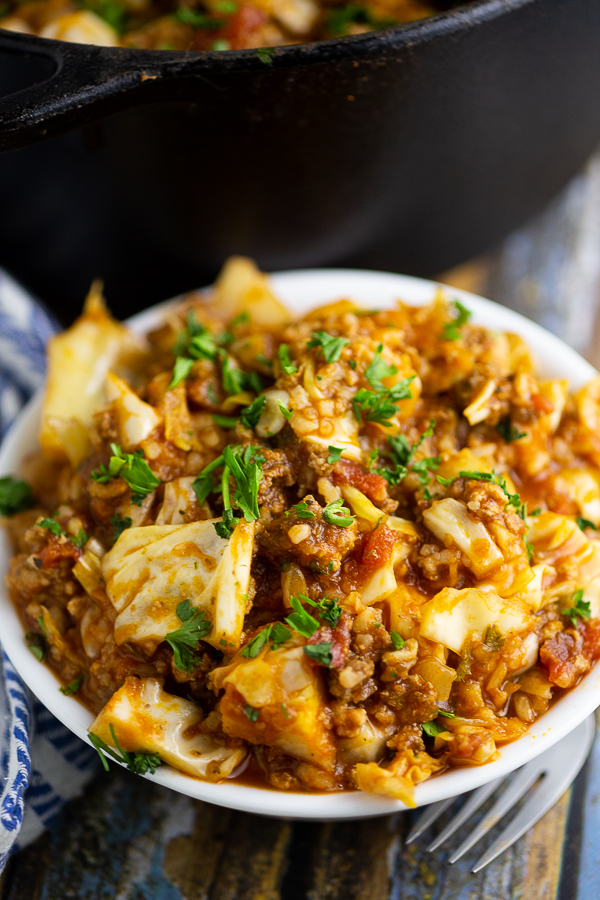 Unstuffed cabbage rolls in a white bowl in front of a black cast iron Dutch oven