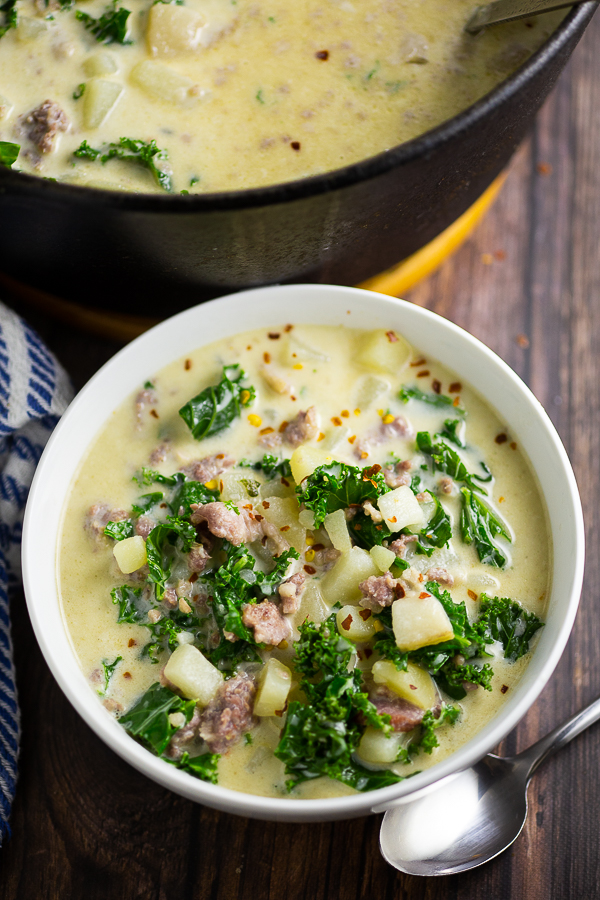 Bowl full of Zuppa Toscana next to a spoon and large pot of soup