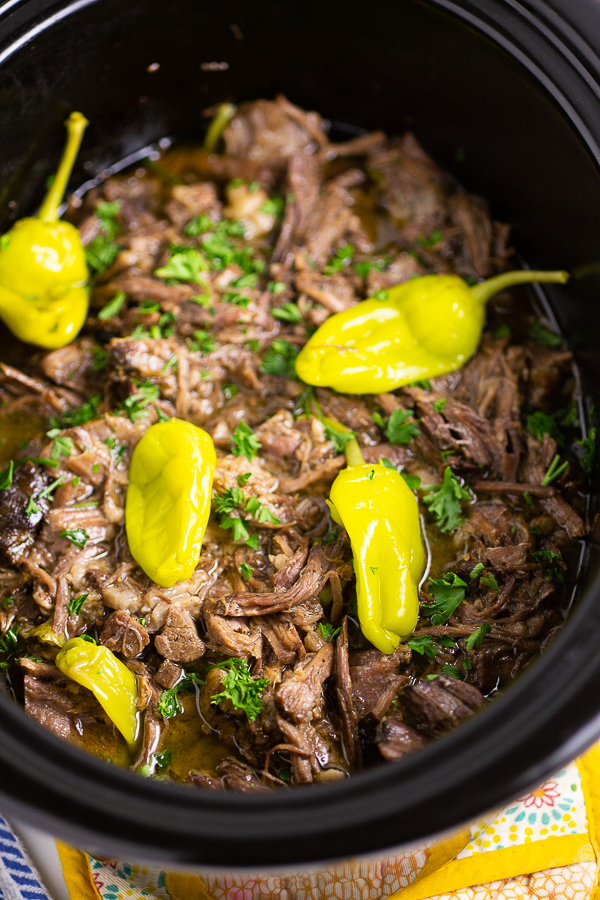 Shredded Mississippi Pot Roast with pepperoncinis and fresh parsley in a slow cooker crock