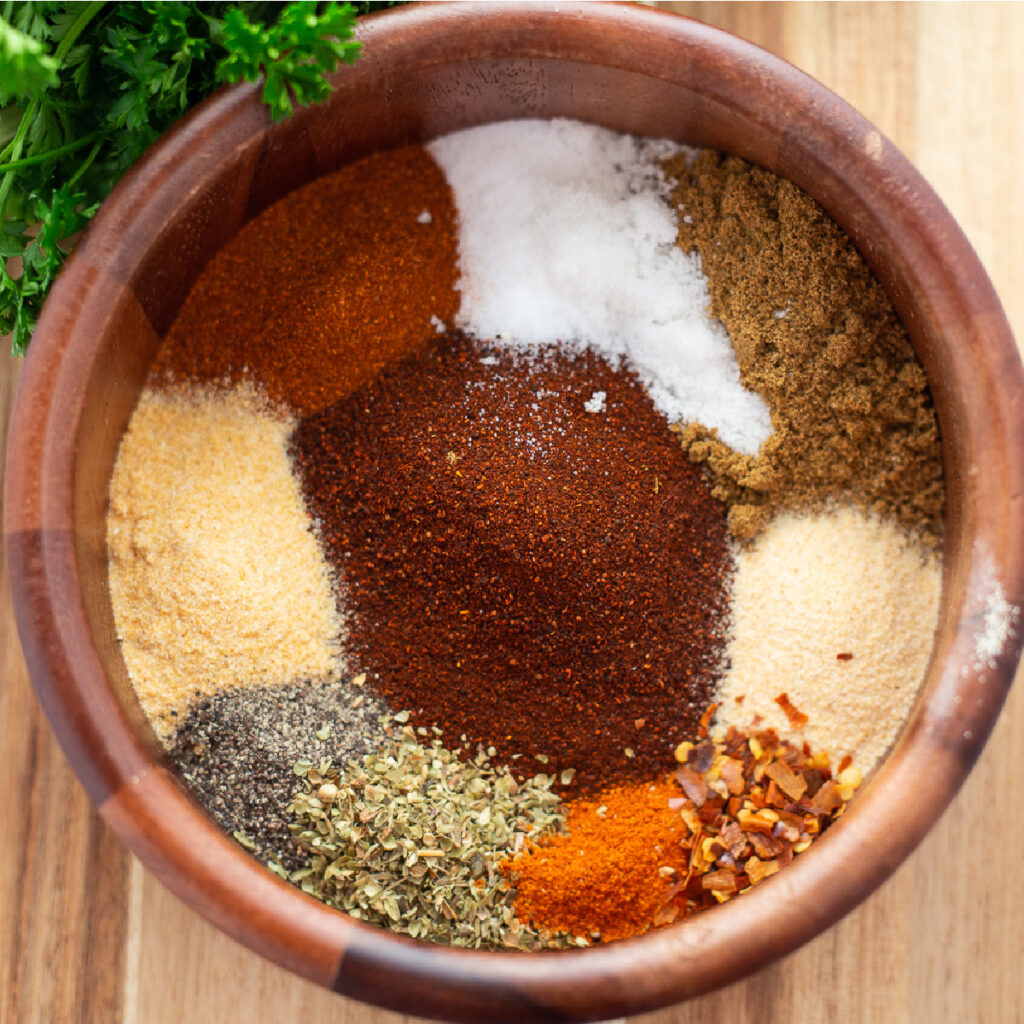 Taco seasoning in a wooden bowl on a wood background next to fresh parsley