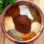 Taco seasoning in a wooden bowl on a wood background next to fresh parsley
