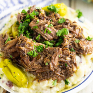 Mississippi mud roast on top of mashed potatoes on a white plate on a rustic wood background