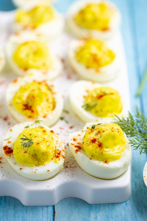 Deviled eggs on a white plate on a blue wood background with fresh dill