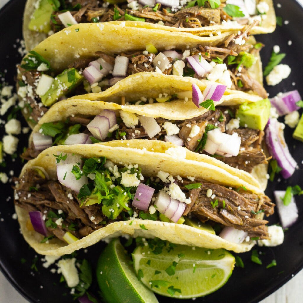 4 street tacos on a black plate stuffed with Chipotle barbacoa, cilantro, redo onion, and queso fresco.