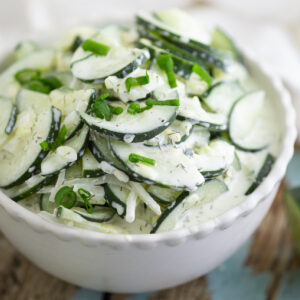 Creamy Cucumber salad topped with fresh chives in a white ceramic bowl sitting on a rustic wood background.