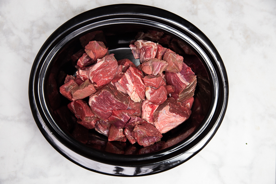 Beef roast cut into bite sized pieces in a slow cooker crock