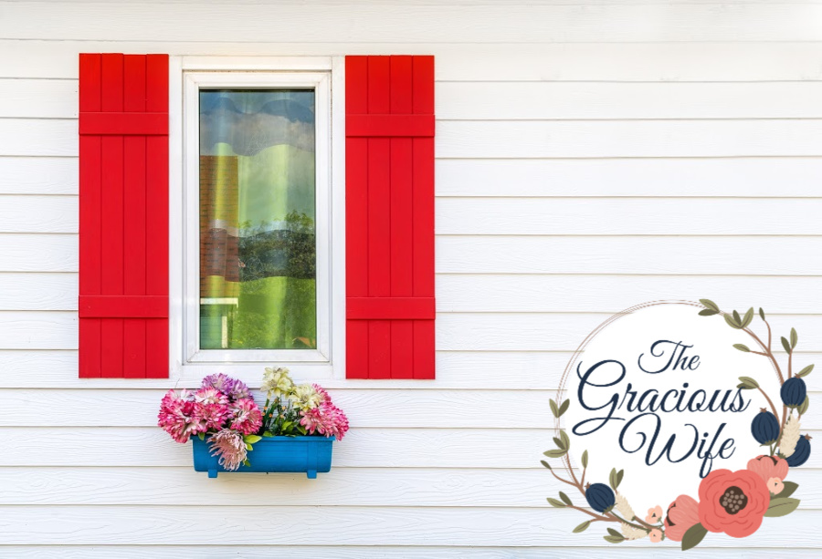 White house with red window shutters, and a bright window basket with flowers