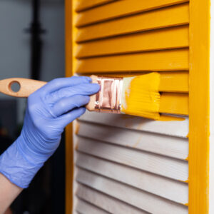 Hand with latex glove painting a door yellow with a paint brush