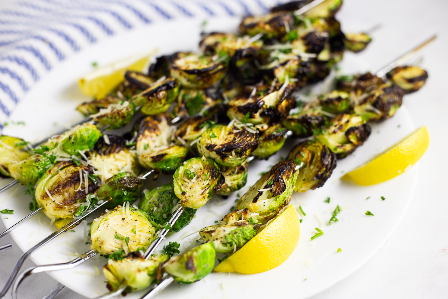Horizontal image of brussels sprouts on a white plate with lemon wedges.