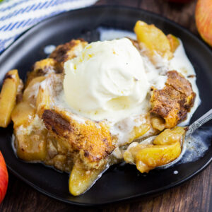 Apple cobbler on a black plate topped with vanilla ice cream