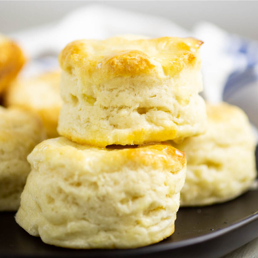 Biscuits stacked on a black matte plate on a white rustic wood background