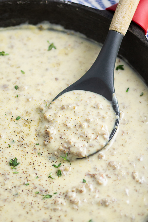 Sausage gravy in a large skillet with a silicone and wood spoon in the middle of it