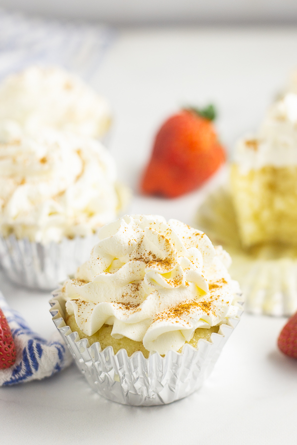 Tres Leches cupcake in a foil wrapper with a strawberry and more cupcakes in the background.