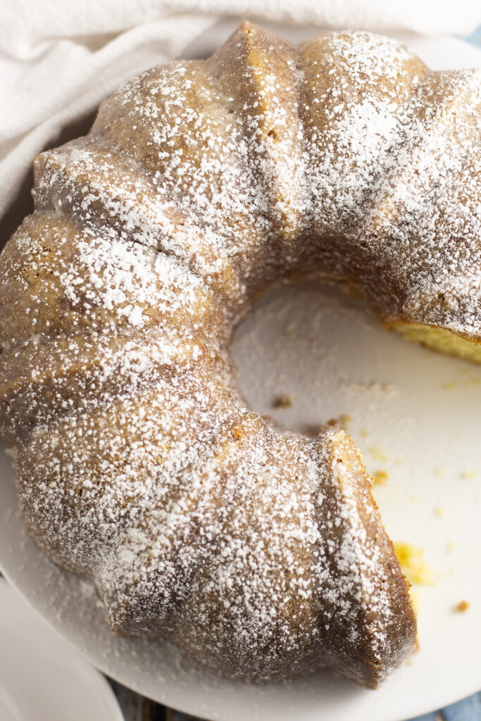 Overhead view of a Kentucky butter cake on a large white plate topped with powdered sugar with a large piece missing