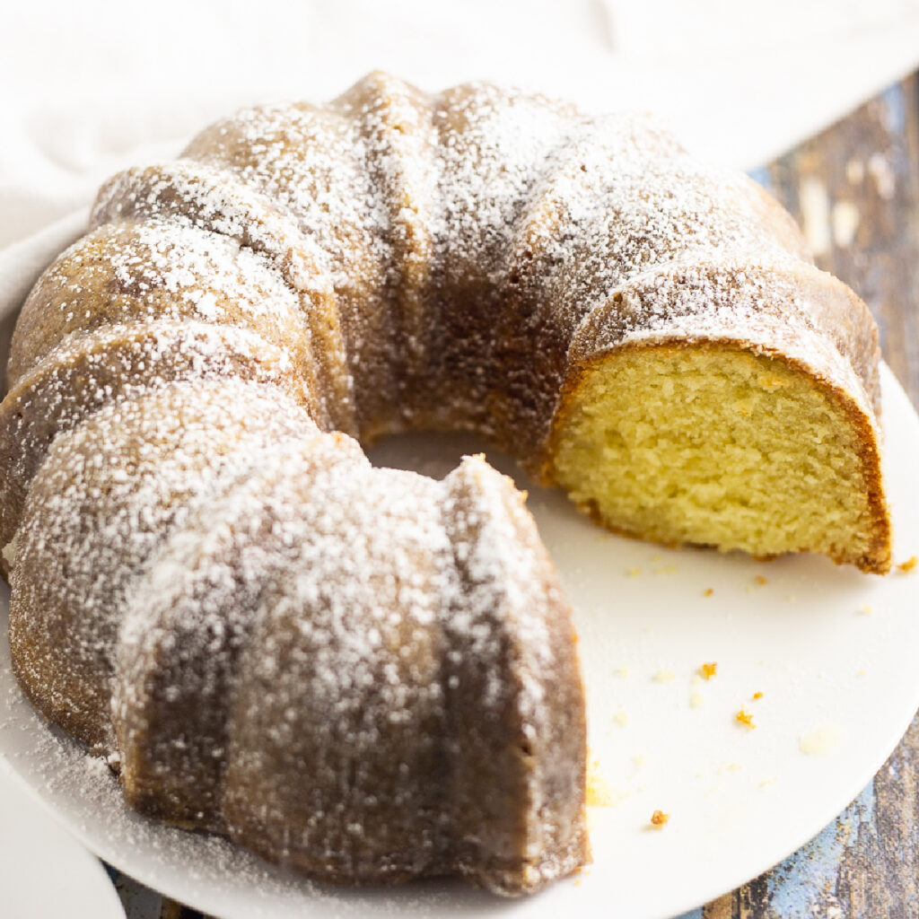 Kentucky butter cake on a large plate with a piece missing and topped with powdered sugar