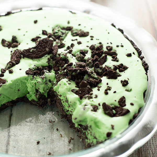 Overhead view of a Grasshopper pie with a slice missing, topped with Oreo crumbles in a glass pie dish